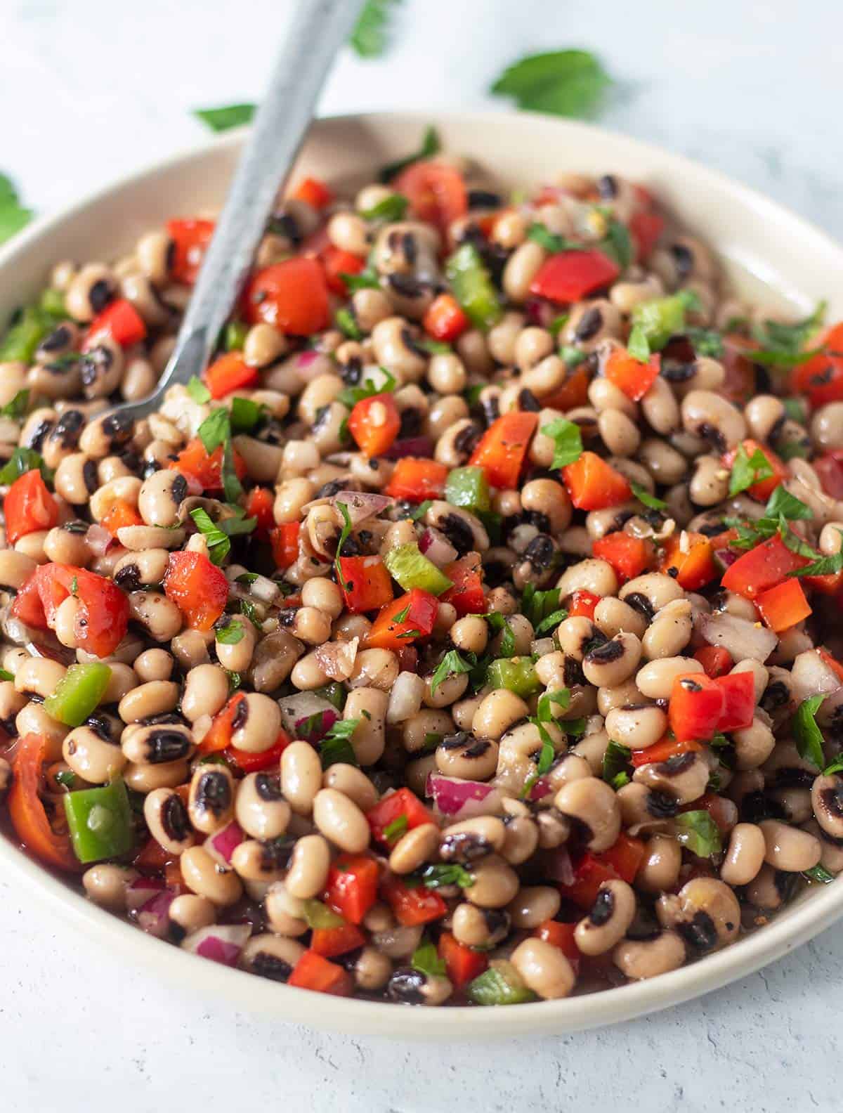 black eyed pea salad in a white salad bowl with a silver serving spoon.