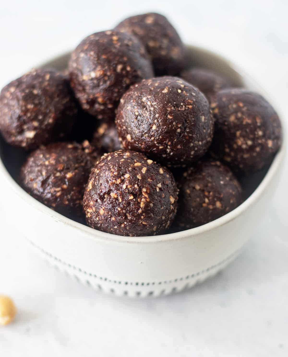 Chocolate protein balls in a white bowl with blue trim and cashews beside the bowl.