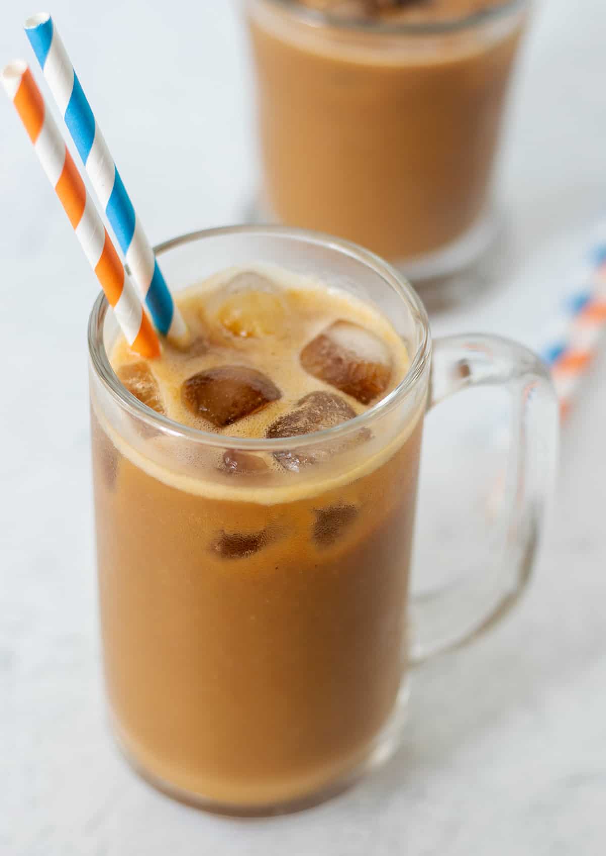 pumpkin coffee smoothie in a tall clear glass with ice. Two straws, one blue and white and one orange and white for serving.