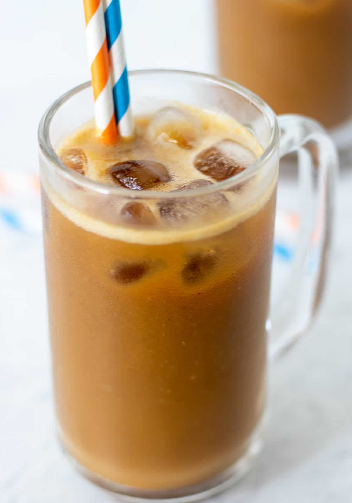 pumpkin coffee smoothie in clear glass with ice and two straws. A blue and white straw and an orange and white straw for serving.