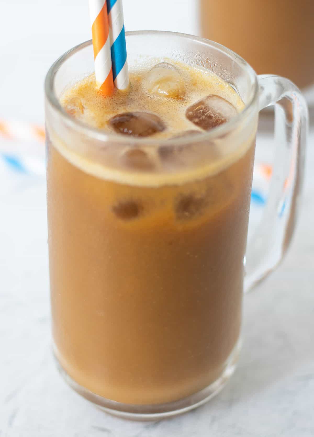 pumpkin coffee smoothie in a clear tall glass with ice. A blue straw and an orange straw in the glass for serving.