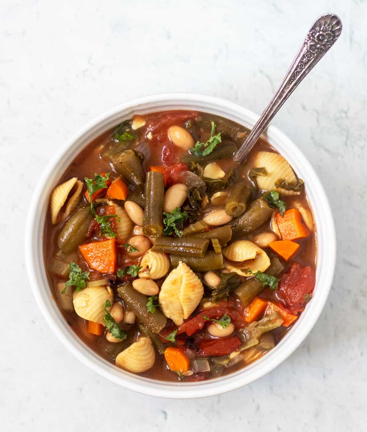 vegetarian minestrone soup in a white bowl with a silver spoon.