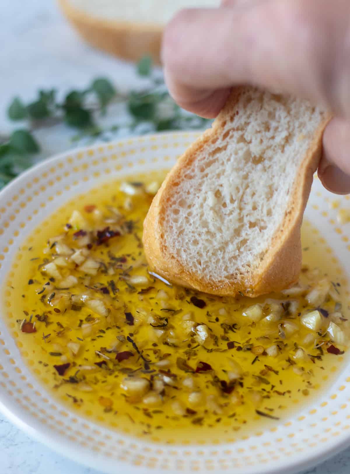 Garlic bread dipping oil on a white and yellow plate with a piece of bread being dunked in the bread oil.