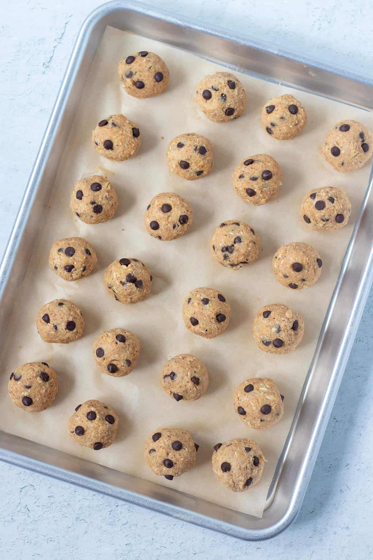 chickpea cookie dough bites rolled into balls with mini chocolate chips. cookie dough balls are on a parchment lined baking tray.