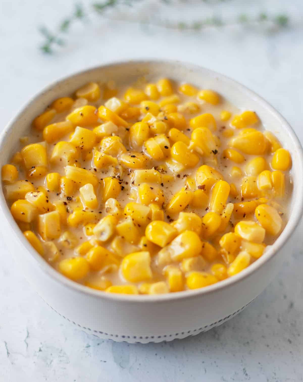 vegan creamed corn garnished with freshly cracked black pepper in a white bowl with blue trim.