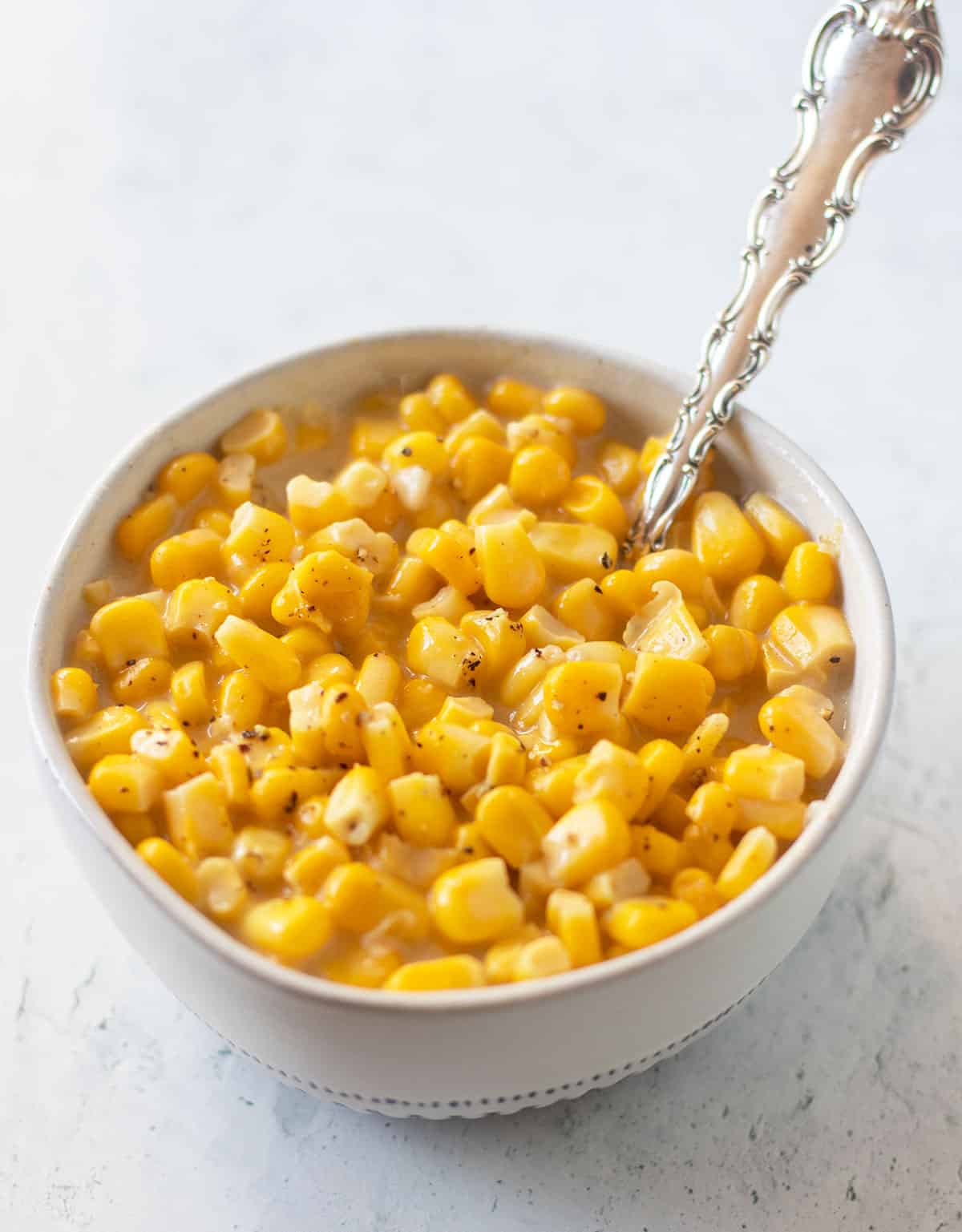 vegan creamed corn in a white bowl with blue trim and a silver spoon for serving.
