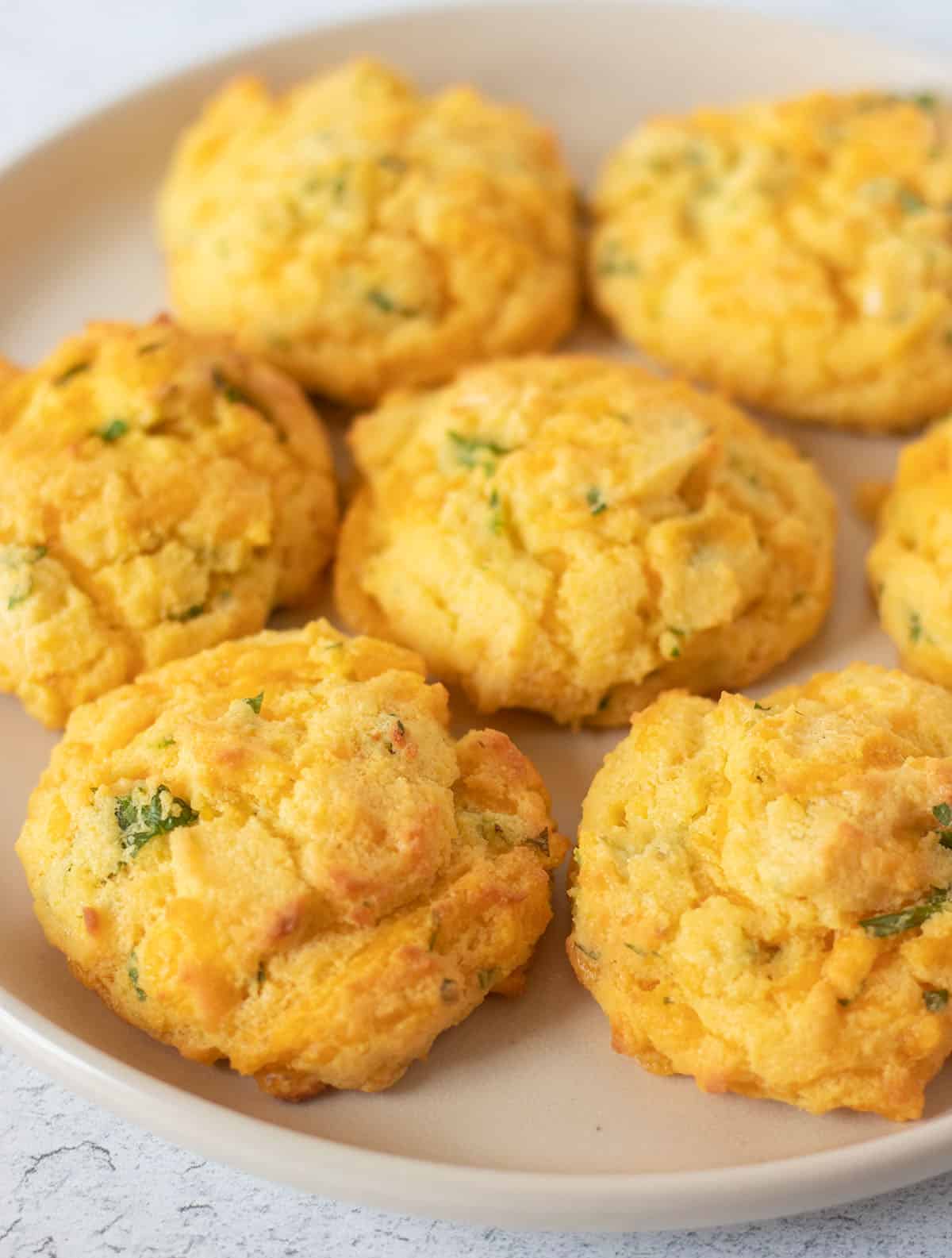Keto coconut flour biscuits with cheddar and parsley served on a beige plate.