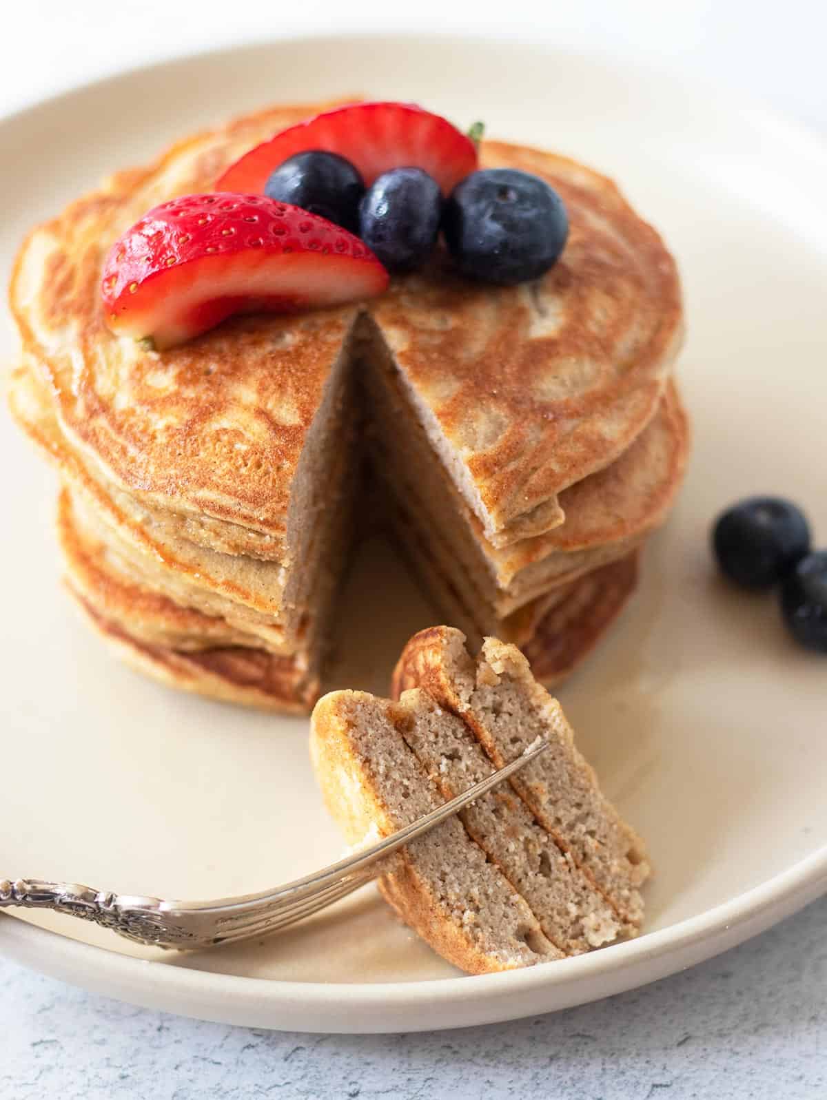 Coconut flour pancakes topped with fresh fruit and cut into a triangle shape pieces on a fork.