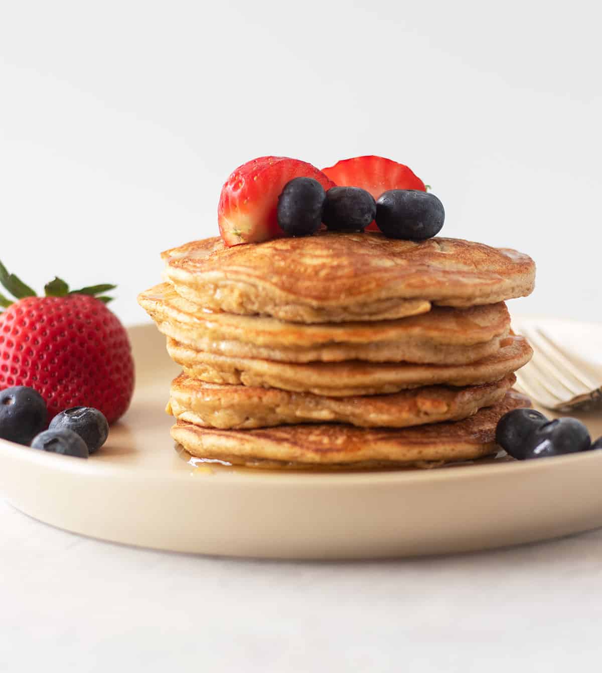 coconut flour pancakes stacked on a beige plate with fresh fruit.