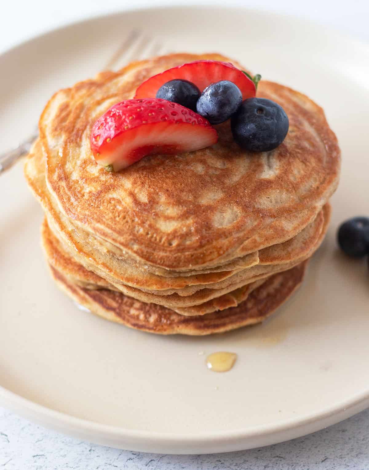 the best coconut flour pancakes stacked on a plate with maple syrup and fresh fruit.