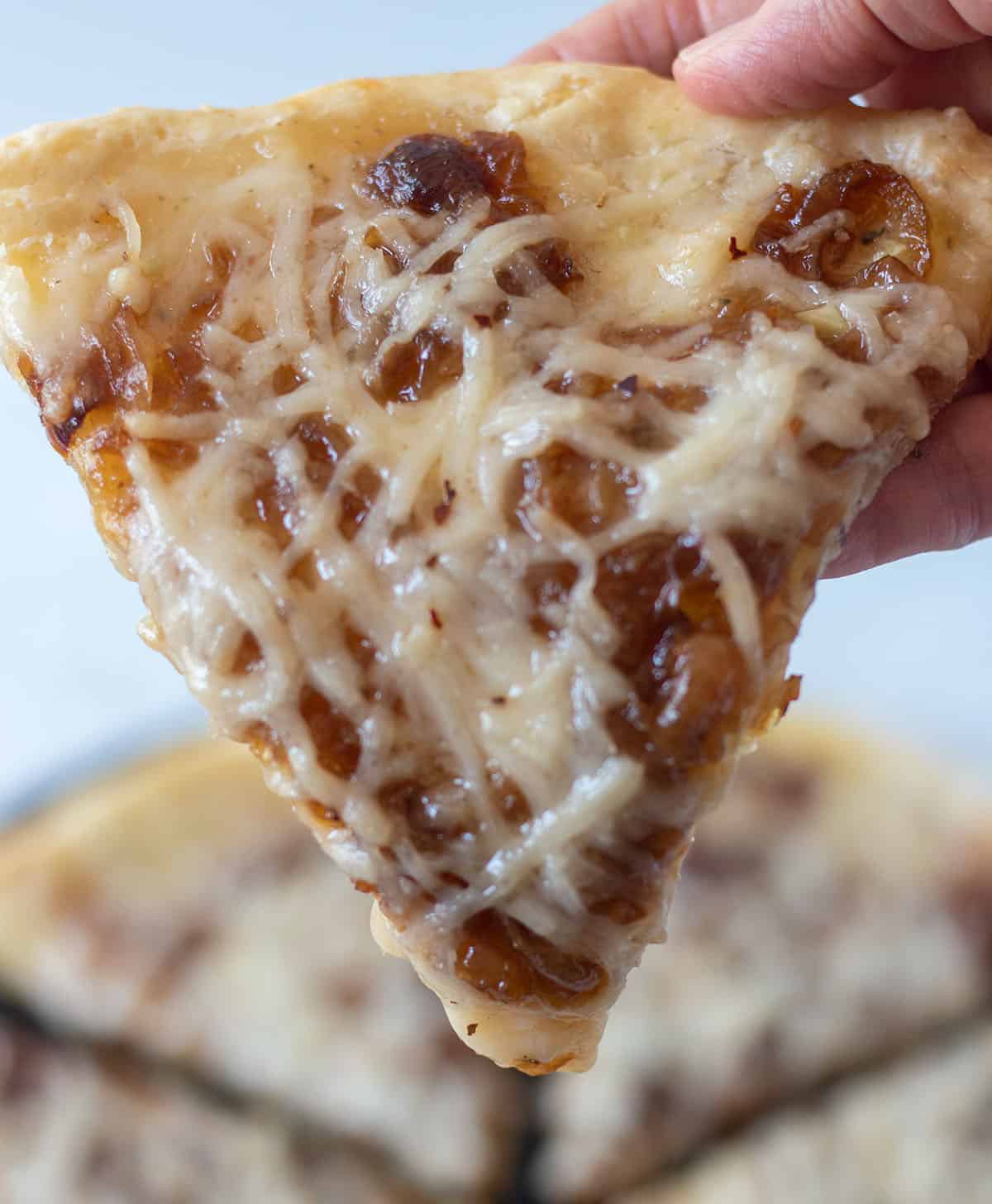 holding a slice of caramelized onion pizza in hand.