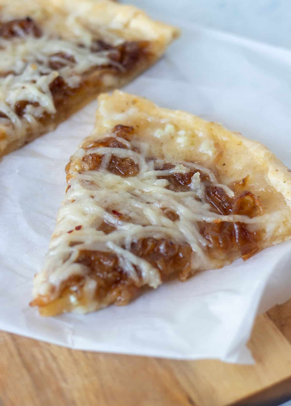 a slice of onion pizza on a cutting board with parchment paper.