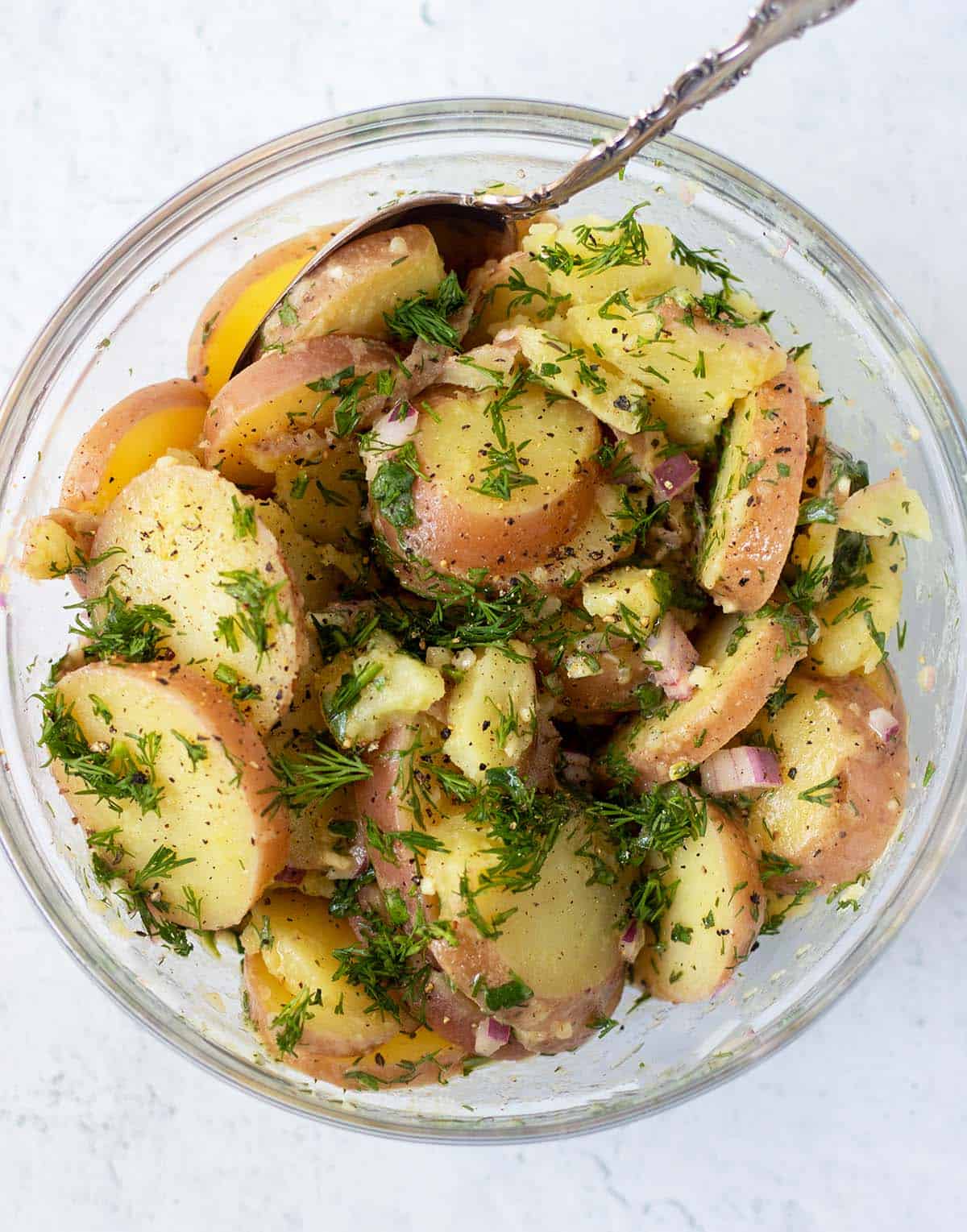 Lemon dill potato salad in large clear glass serving bowl with silver serving spoon.