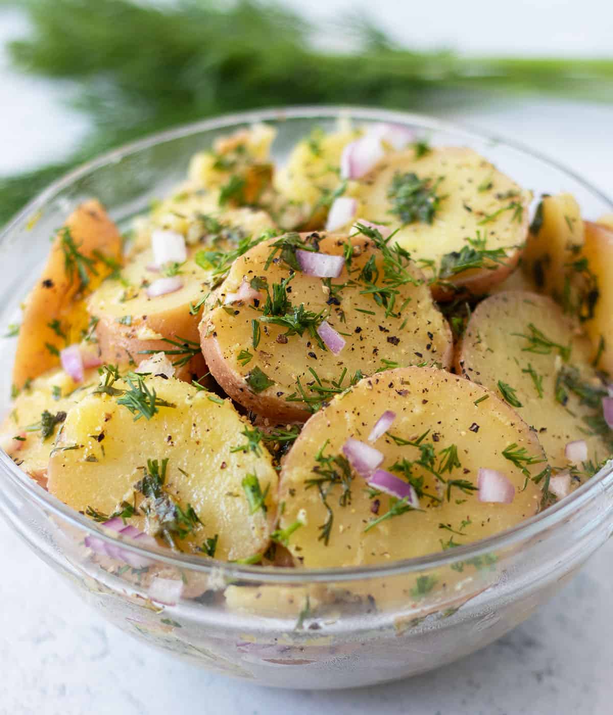 dill potato salad in a clear glass serving bowl topped with fresh chopped dill weed.