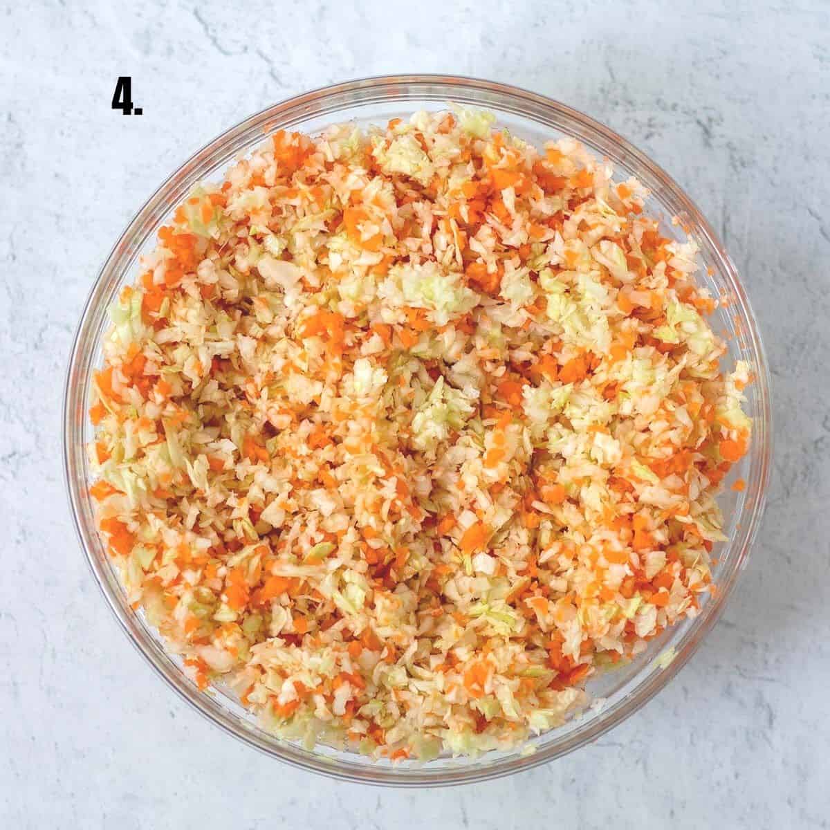 shredded carrots and cabbage mixed together in glass mixing bowl.