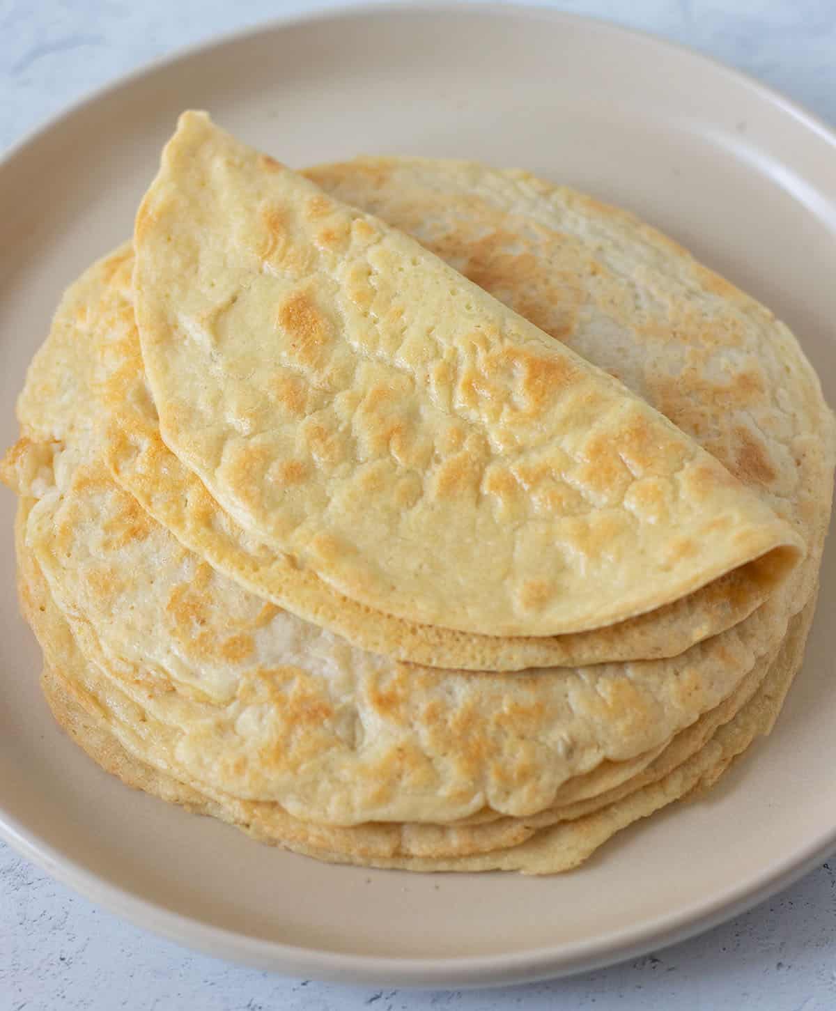 almond flour tortillas stack on a beige plate with the one on top folded over.