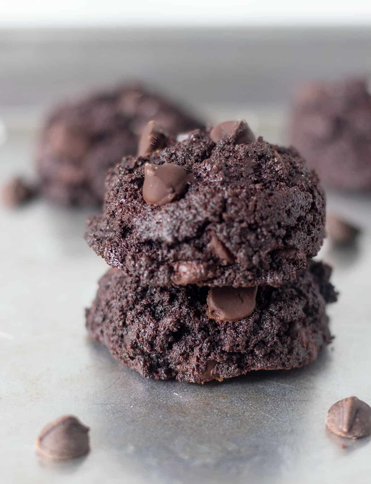 two chocolate coconut flour cookies stacked on top of each other on a silver baking pan.