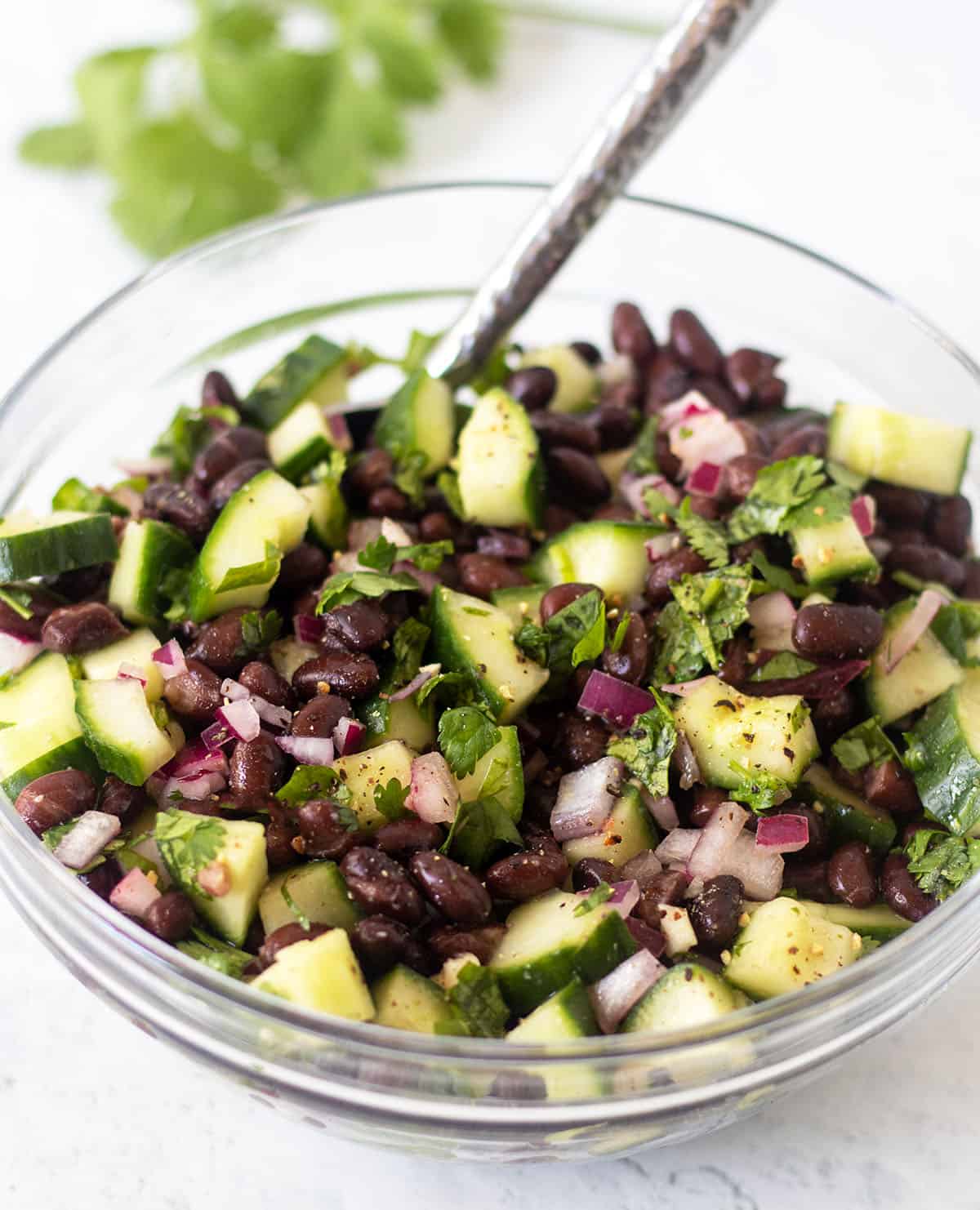 cucumber black bean salad in a clear glass bowl with a silver spoon for serving.