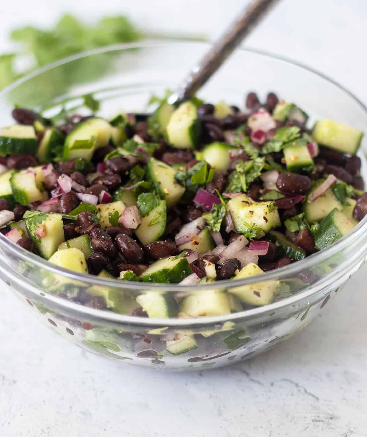 Cucumber black bean salad in glass bowl with silver spoon for serving.