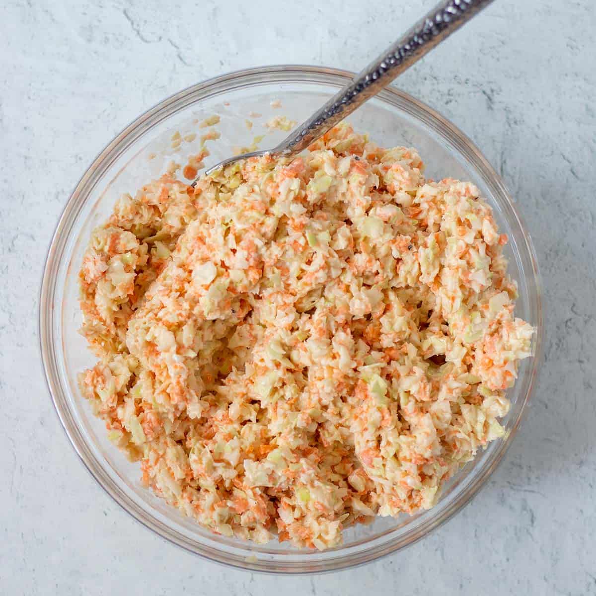 Prepared honey mustard coleslaw in a clear mixing bowl with a silver spoon.
