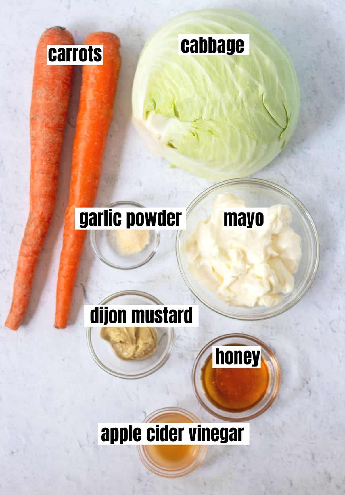 ingredients for honey mustard coleslaw which include carrots, cabbage, mayo, dijon mustard, honey, apple cider vinegar, and garlic powder.