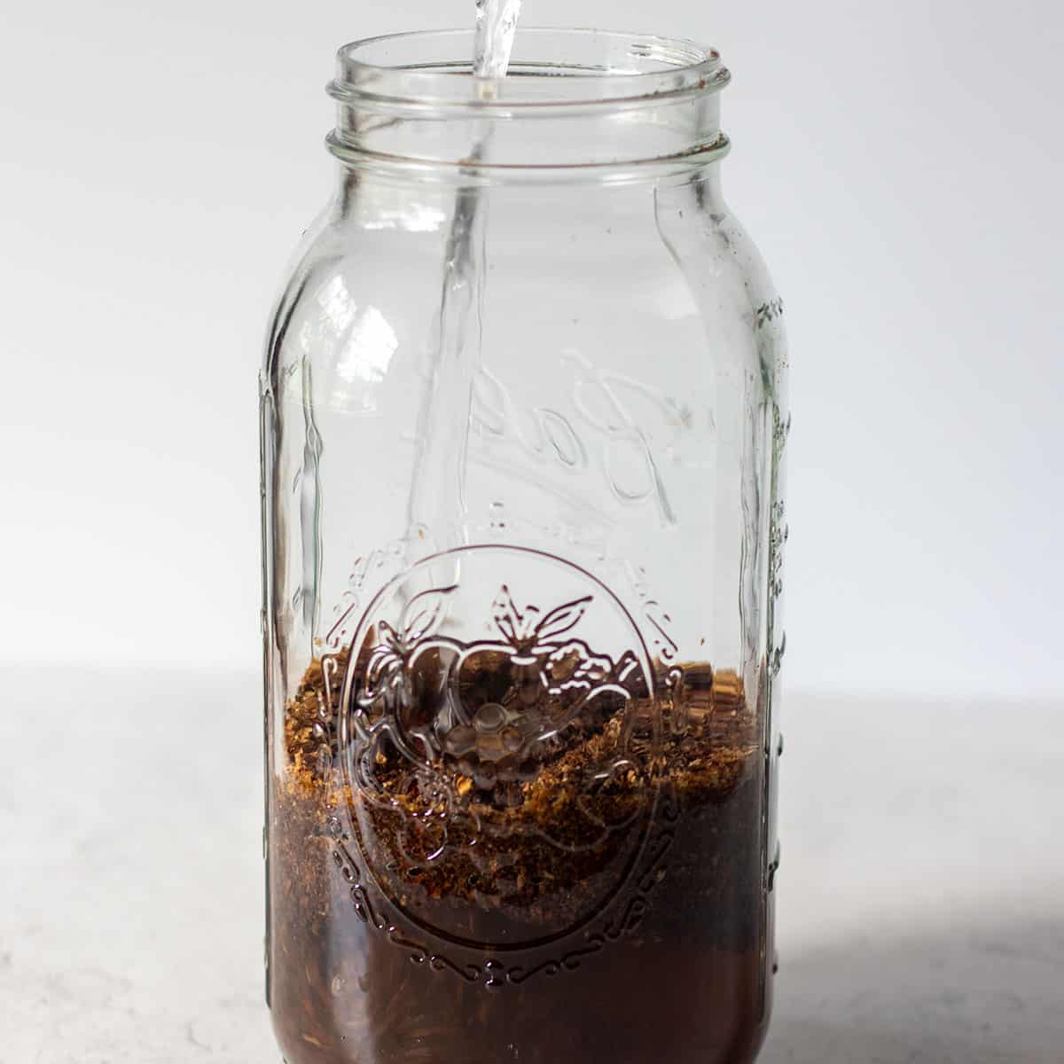 water being added to coffee grinds in mason jar.