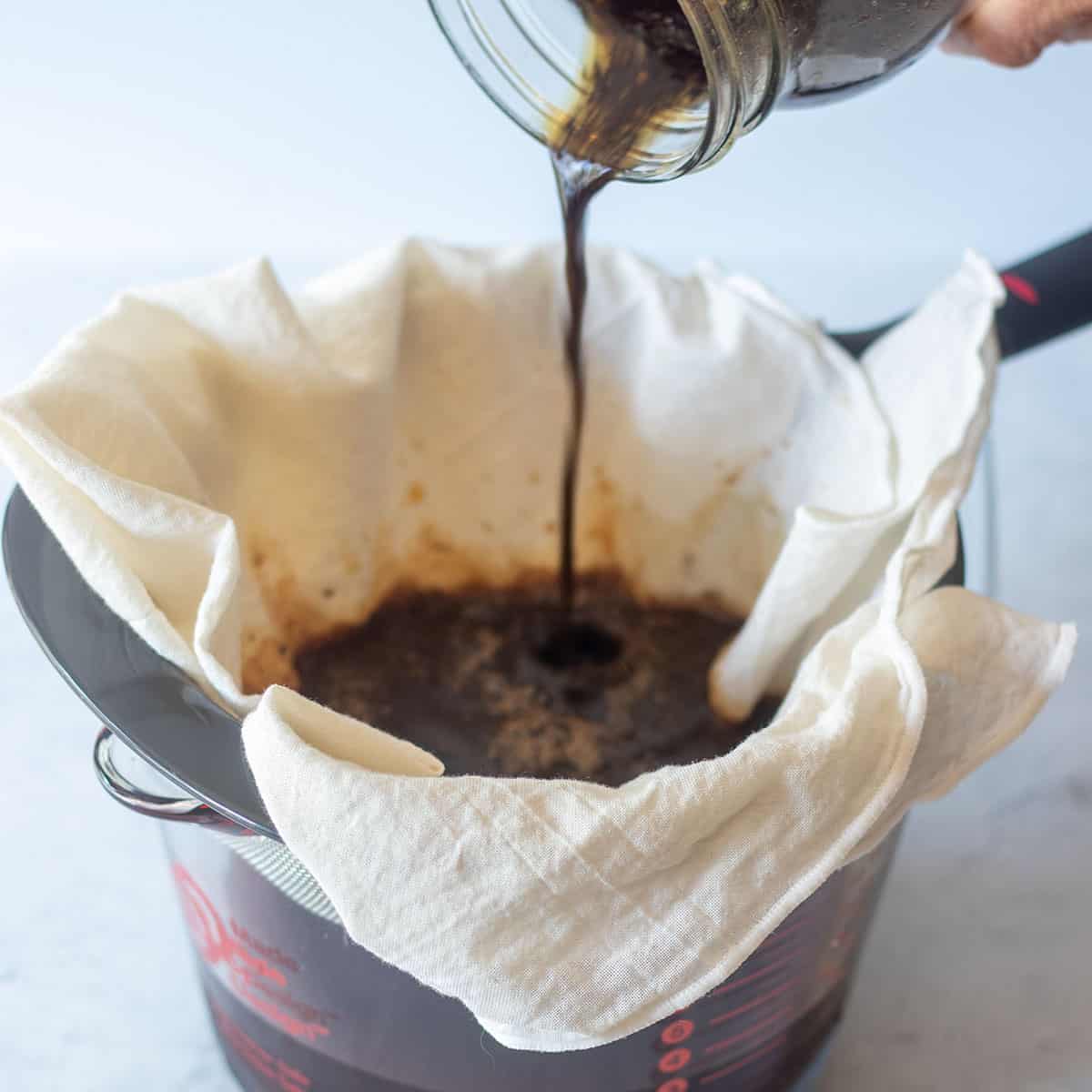 pouring cold brew coffee through a mesh strainer lined with cheesecloth.
