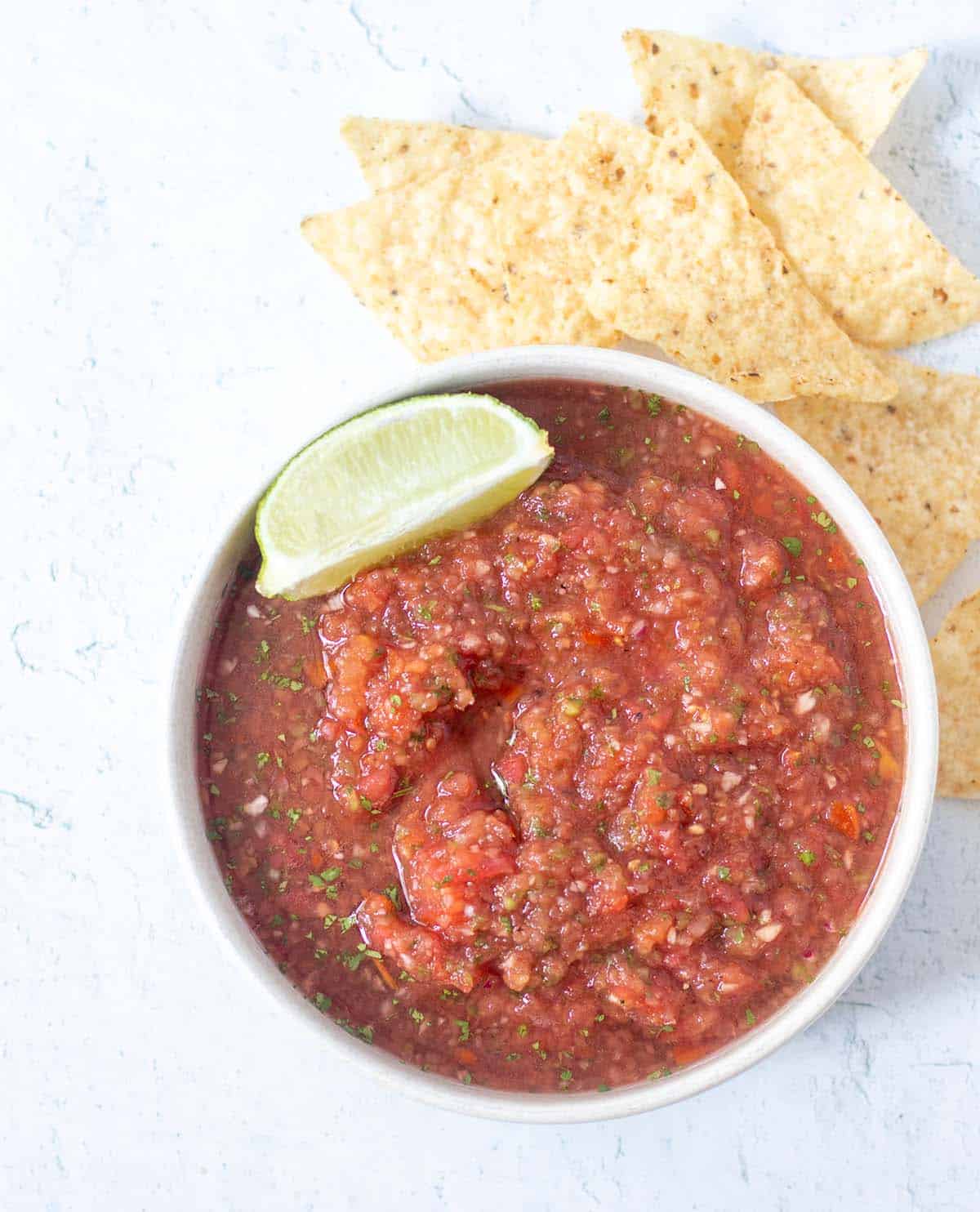Homemade salsa in a white bowl with a lime wedge and tortilla chips beside the bowl.