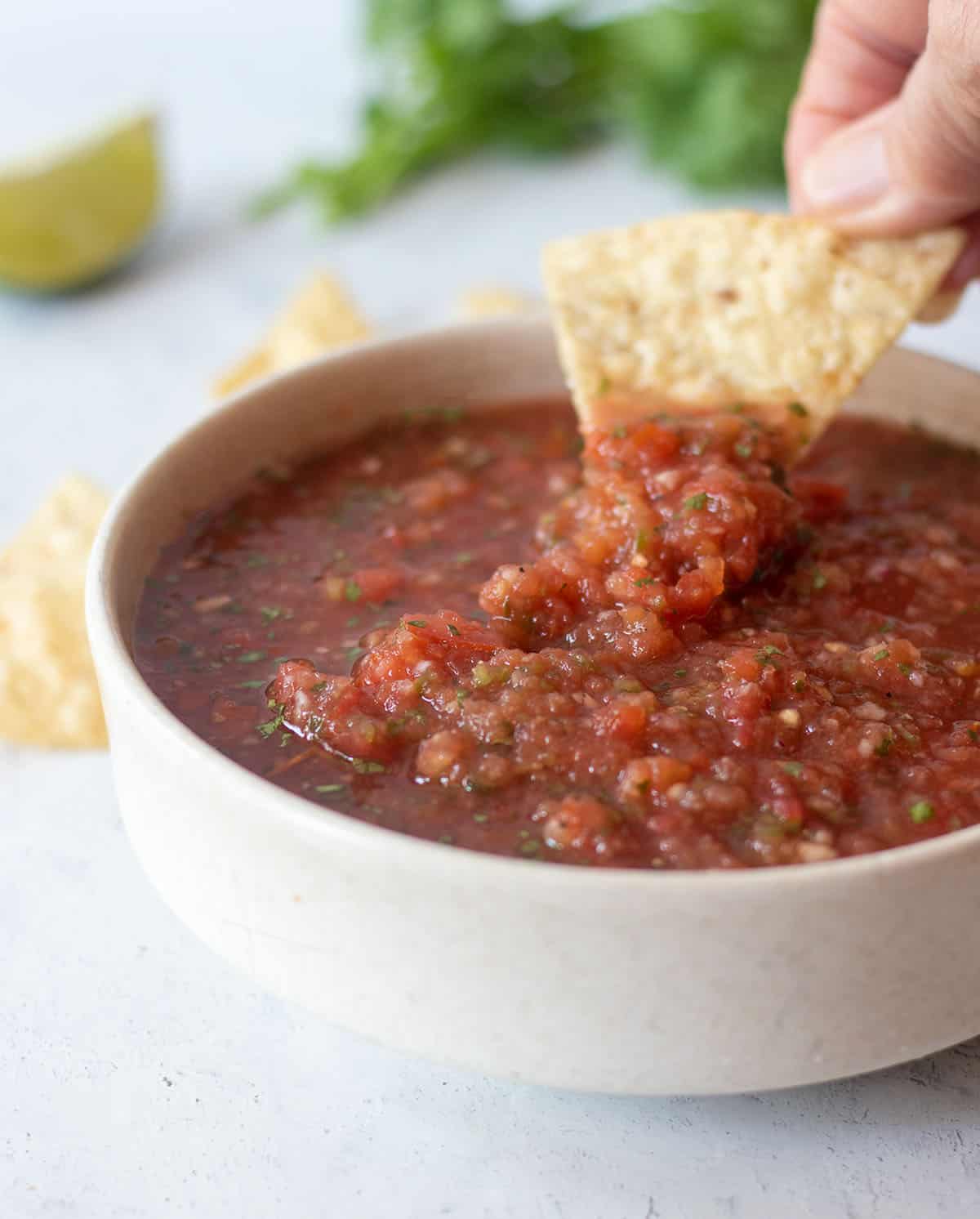 Homemade salsa in a white bowl with a tortilla chip dipping some salsa on it.