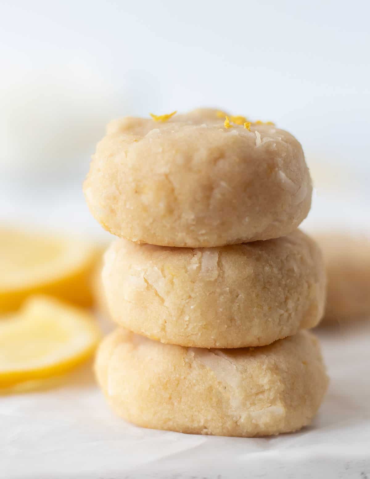 three soft lemon cookies stacked on top of each other with lemon slices in the background.