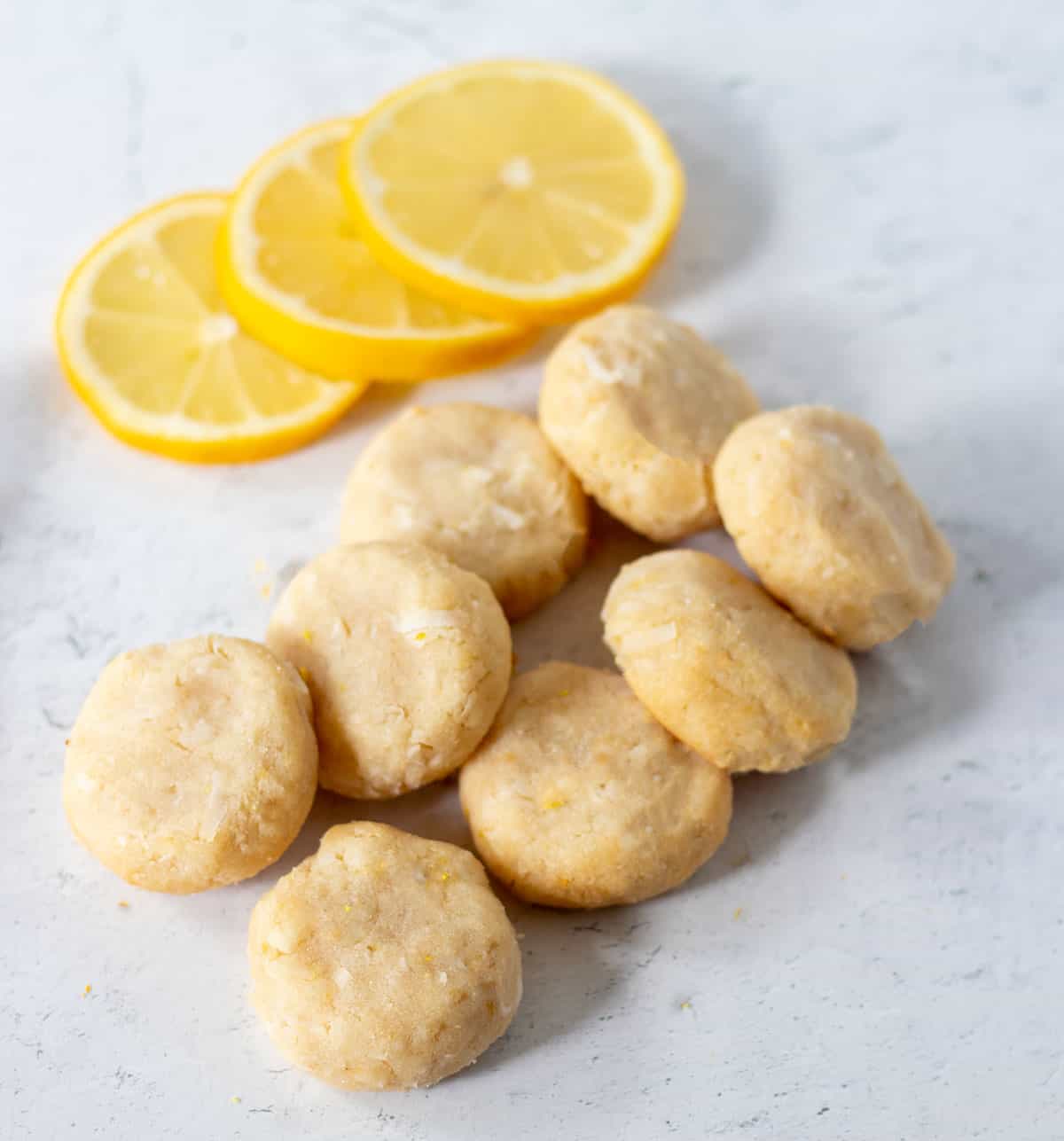 baked lemon cookies on counter with three fresh lemon slices.