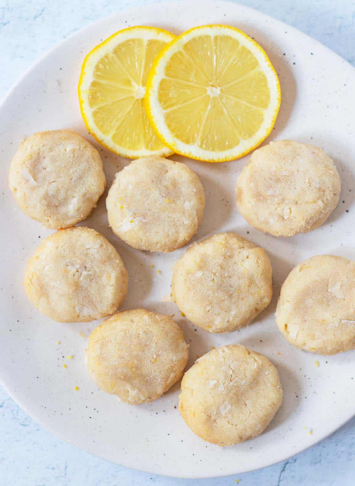 Soft lemon cookies on a white plate with fresh lemon slices.