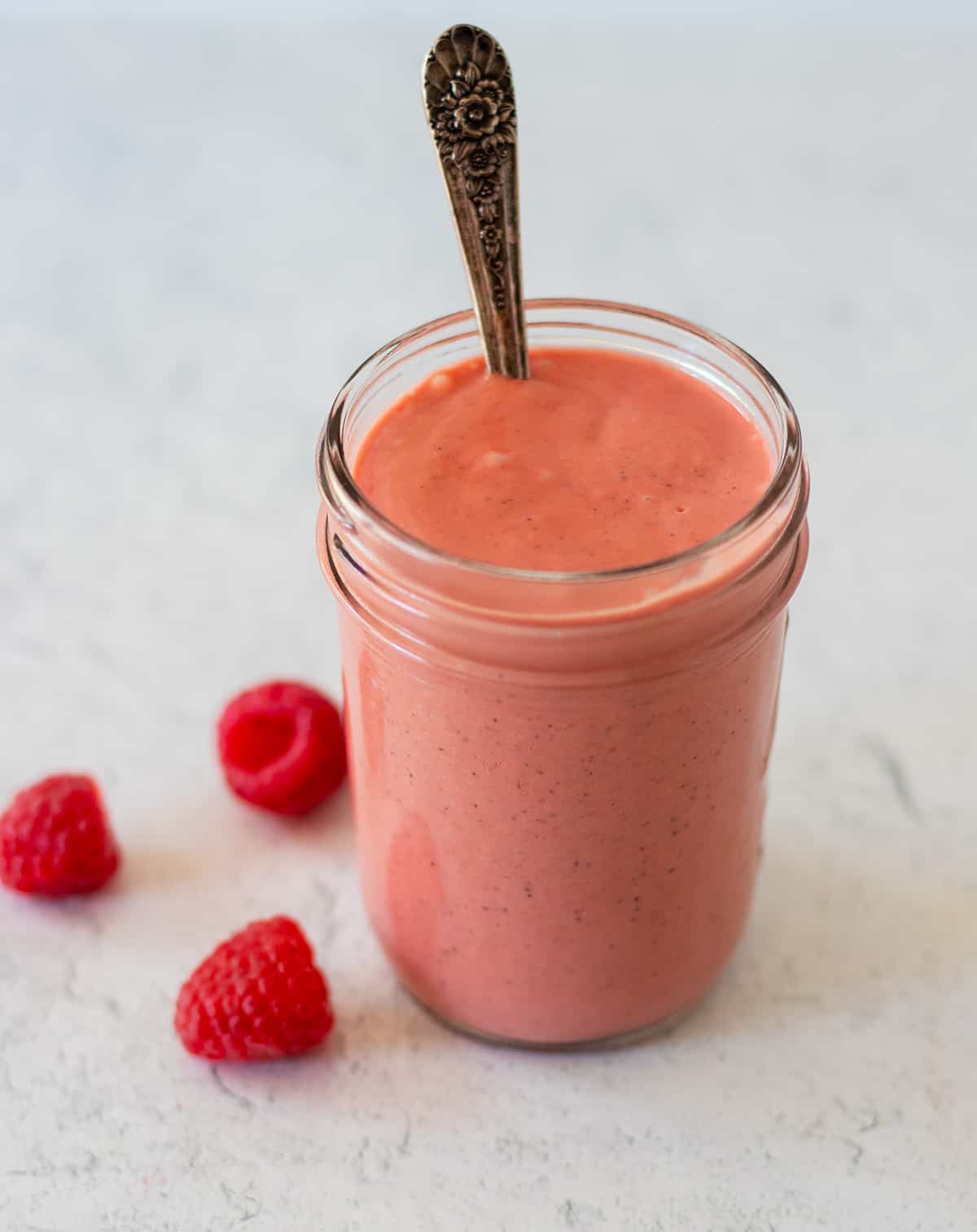 Raspberry vinaigrette in a glass jar with a silver spoon.