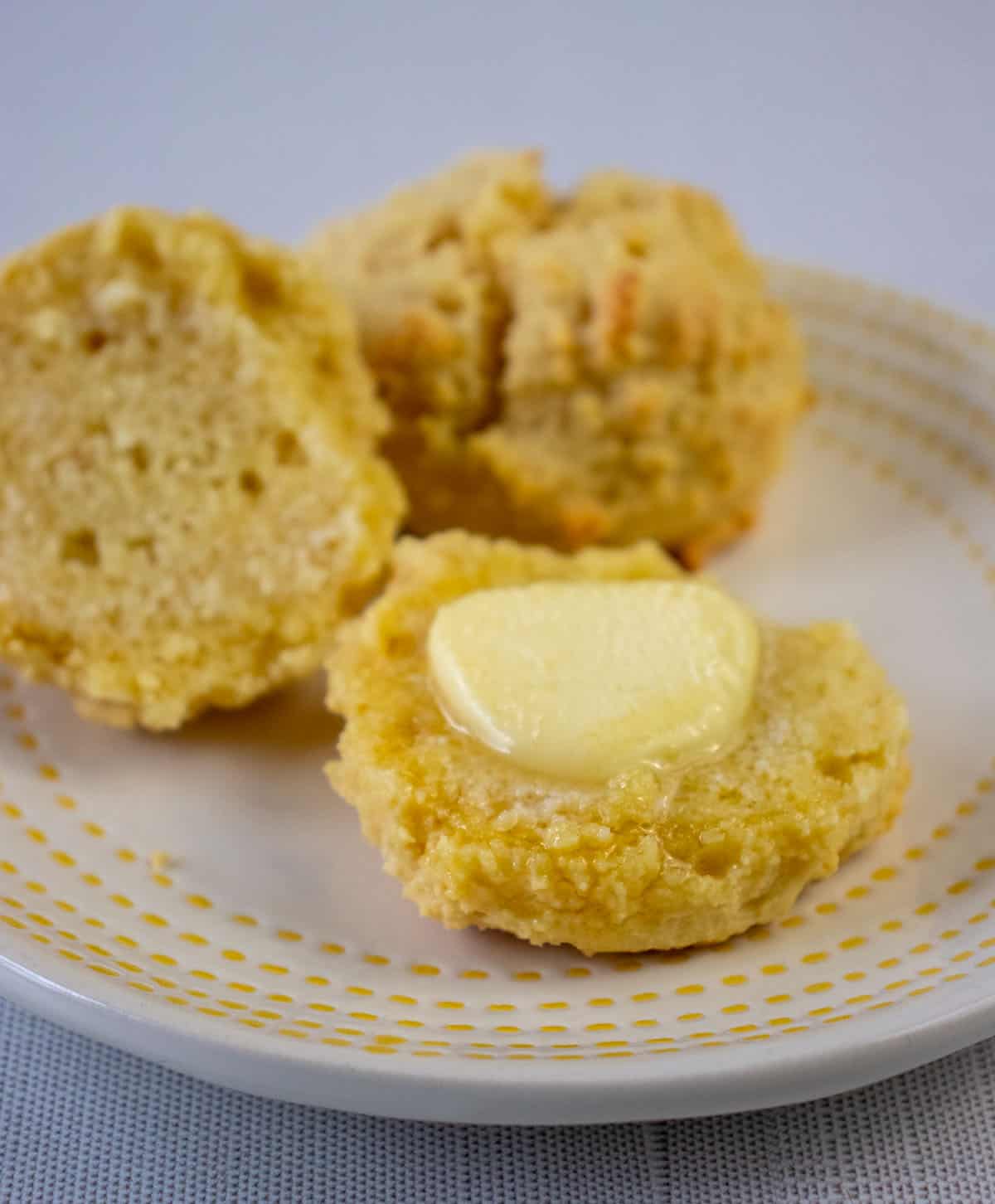 almond flour biscuits on a white plate with yellow trim. One biscuit slice in half with melted butter on it.
