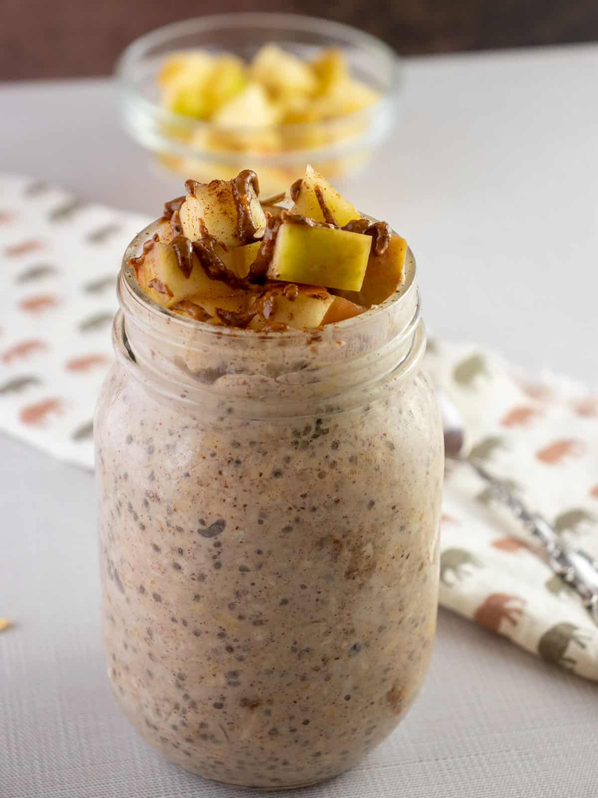 apple cinnamon overnight oats in a glass mason jar topped with extra apples, almond butter and cinnamon.