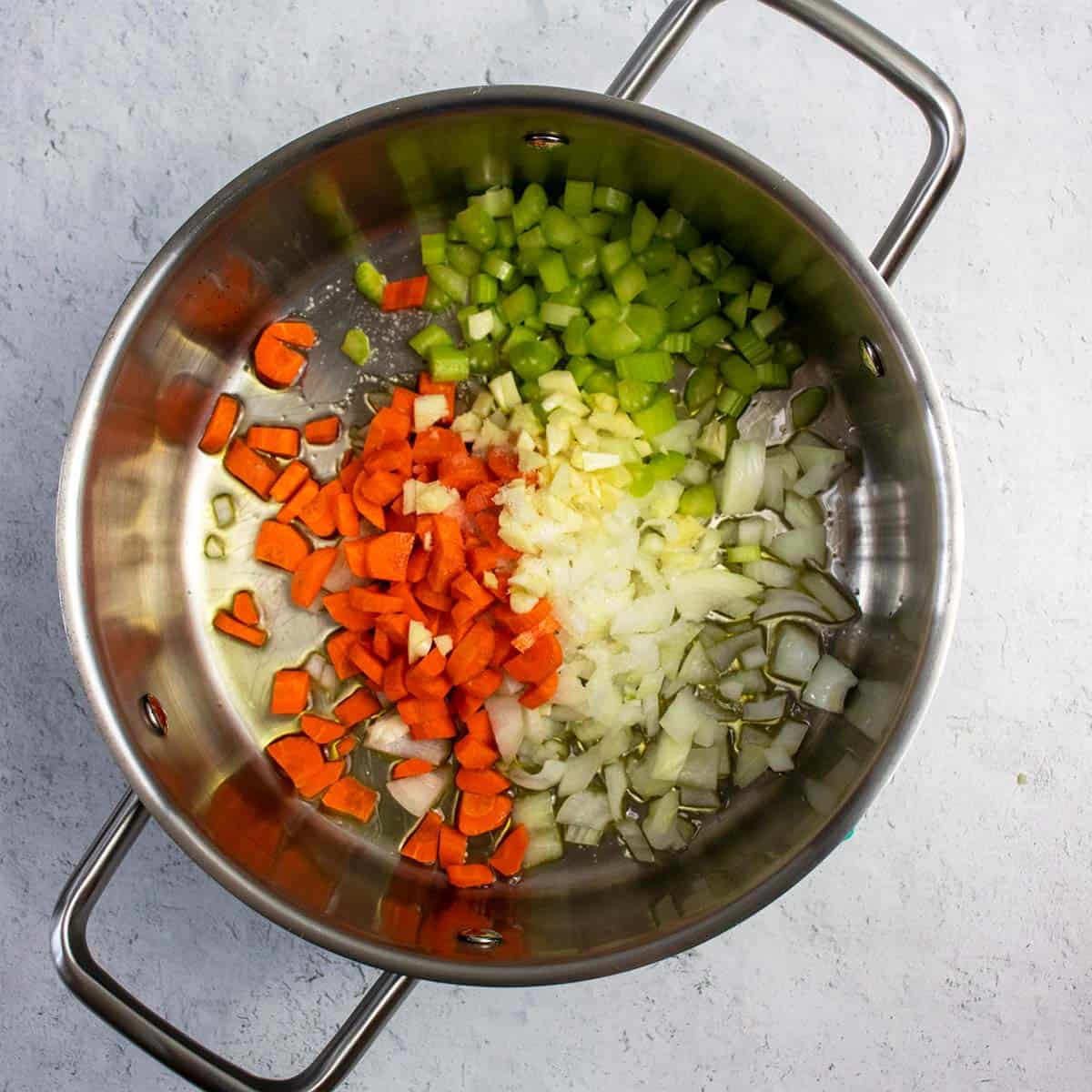 Diced carrots, onions, celery and garlic being sautéed in soup pan for vegan tomato soup.