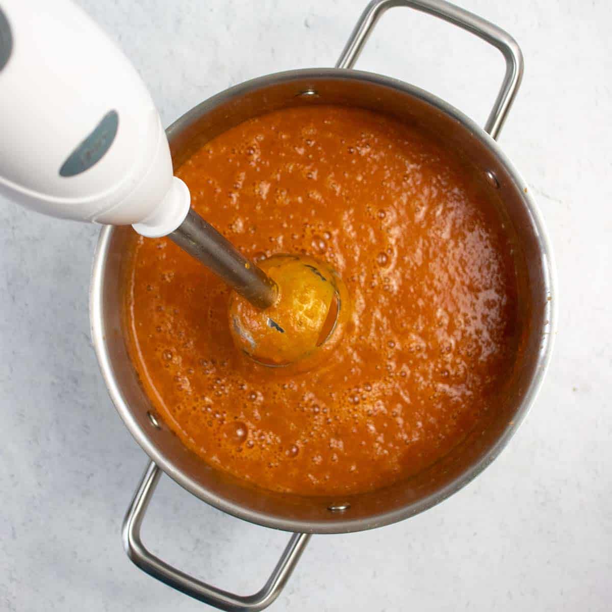 Vegan tomato soup being puréed with an immersion blender.