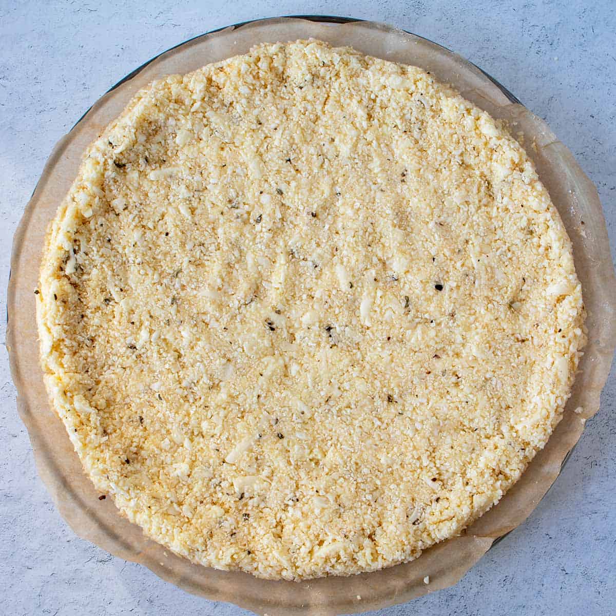 cauliflower pizza crust spread out on parchment paper prior to baking.