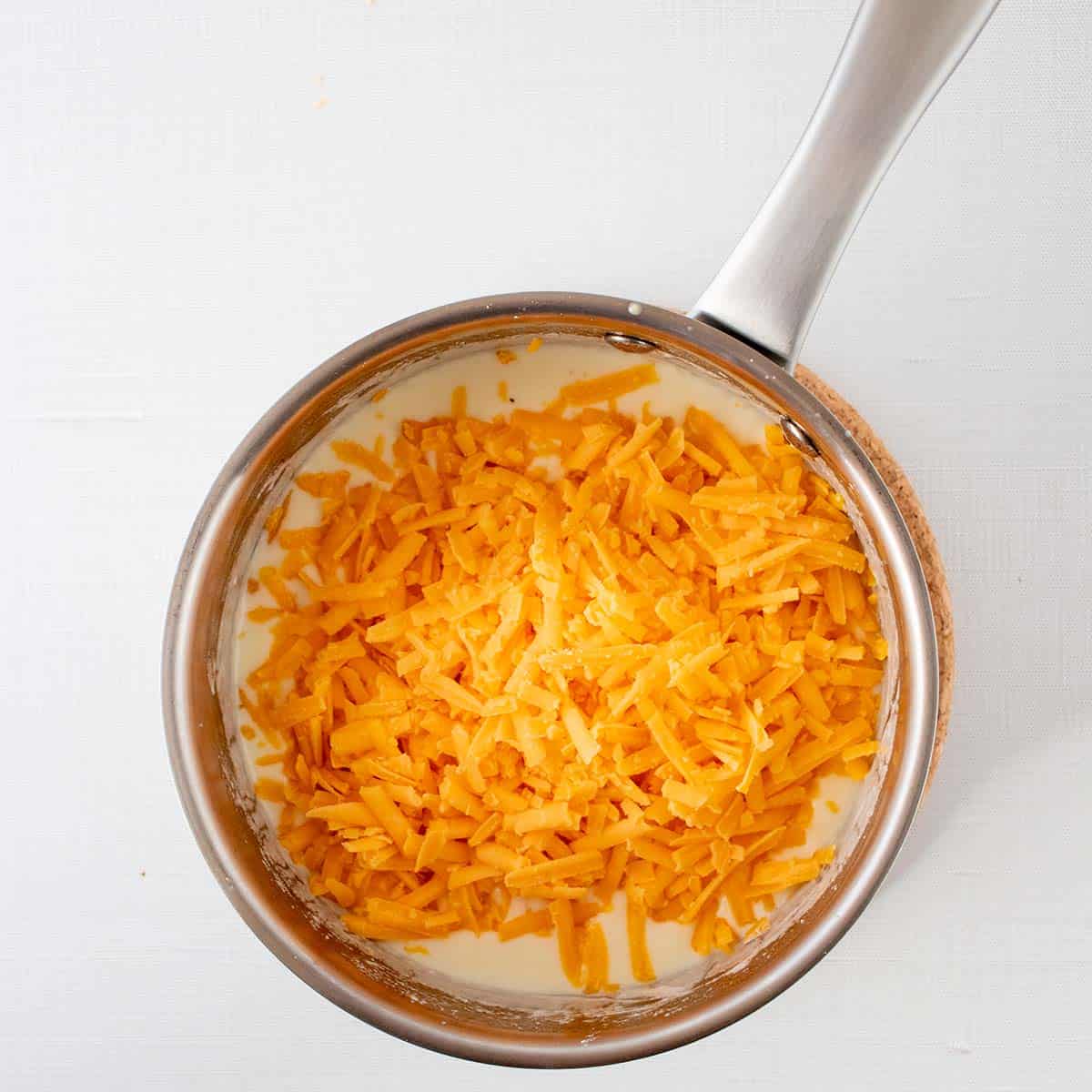 shredded cheese added to cream mixture in saucepan.
