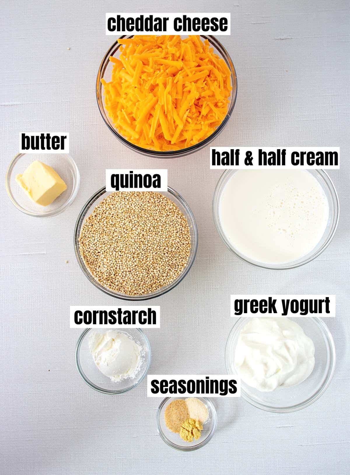 ingredients for cheesy quinoa which include cheddar cheese, butter, quinoa, half & half cream, cornstarch, greek yogurt, & seasonings.