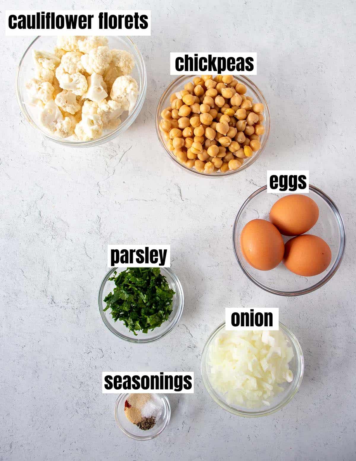 chickpea burger ingredients including cauliflower florets, chickpeas, eggs, onion, parsley, & seasonings.