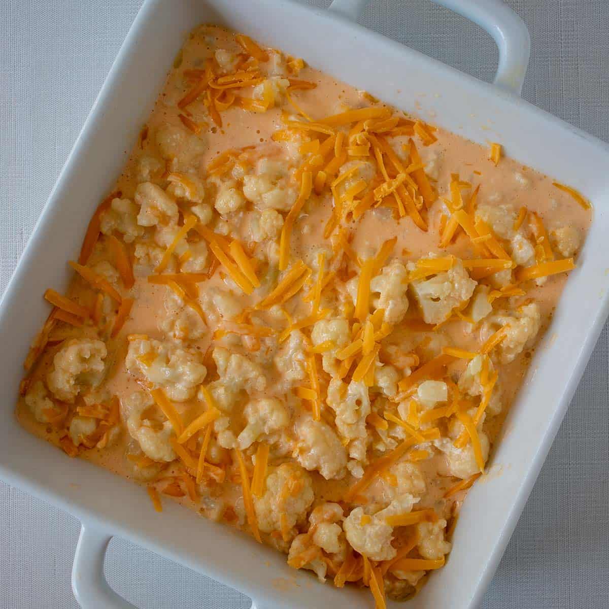 cauliflower mac and cheese mixture poured into casserole pan and topped with additional cheese prior to baking.